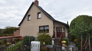 Ein zweistöckiges Haus mit geneigtem Dach, einer Veranda und einem kleinen Garten.