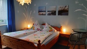 A bedroom with a wooden bed, a bedside table with a lamp, a chair, and wall art.