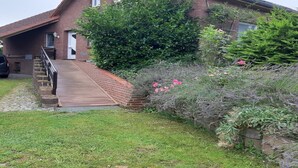 A brick house with a wooden staircase leading to the front door, surrounded by a garden with various plants and flowers.
