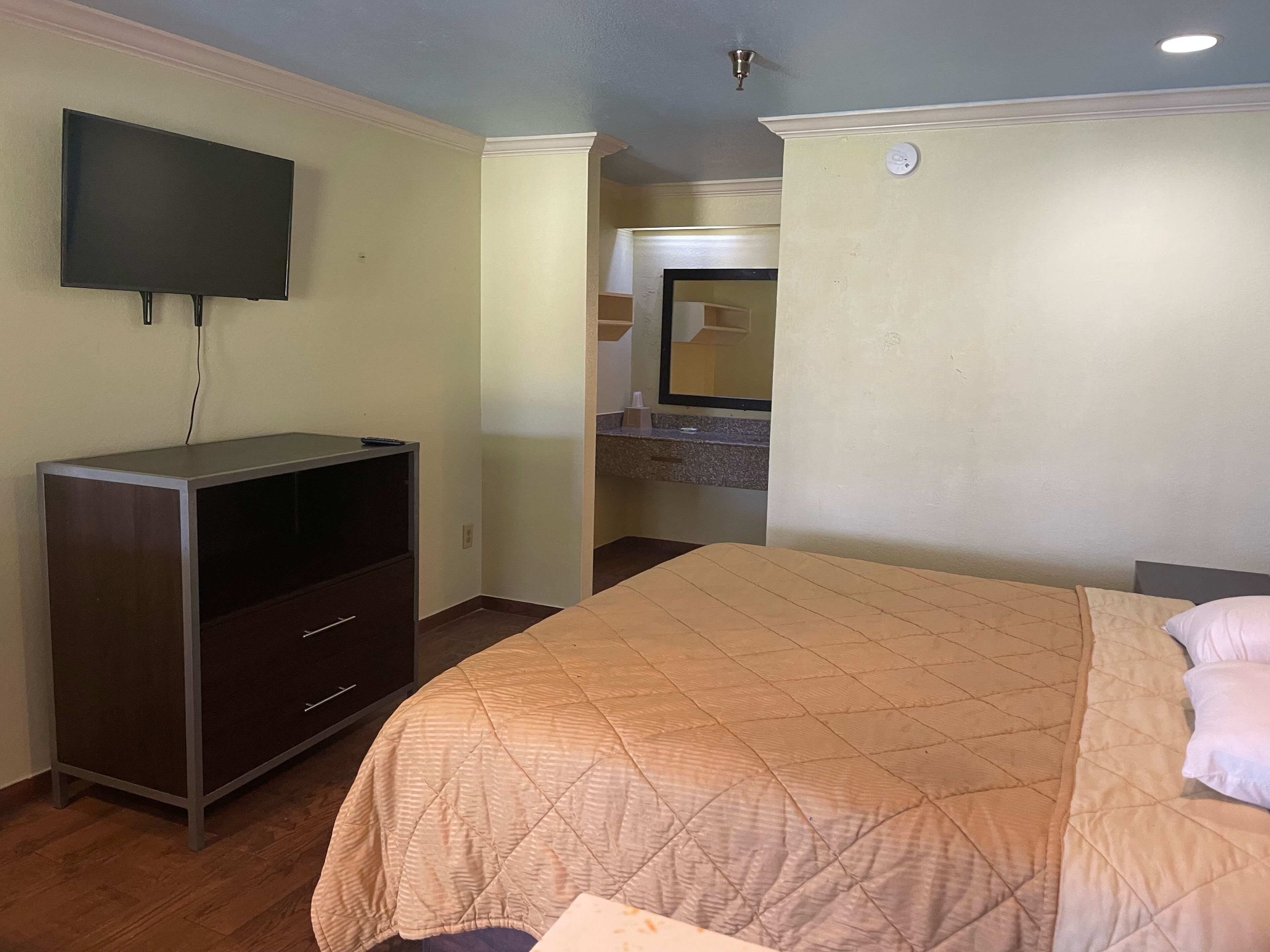 Une chambre d’hôtel avec un lit, un téléviseur fixé au mur, une commode et une salle de bain visible à travers une porte ouverte.