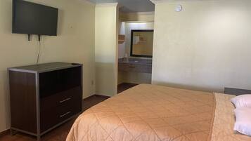 Une chambre d’hôtel avec un lit, un téléviseur fixé au mur, une commode et une salle de bain visible à travers une porte ouverte.
