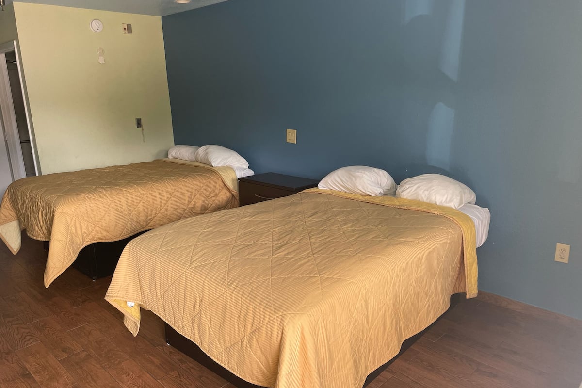 Dos camas individuales con ropa de cama color beige, suelo de madera y pared azul.