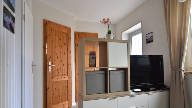A room with a wooden door, a white cabinet with drawers, a television, and a window with curtains. - Ferienwohnung auf dem Land in Strandnähe (Kröpelin / OT Diedrichshagen)