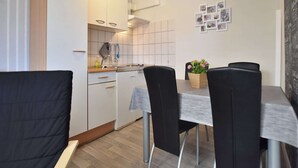 A compact kitchen with white cabinets, a sink, and a dining area with a table and chairs. - Ferienwohnung auf dem Land in Strandnähe (Kröpelin / OT Diedrichshagen)