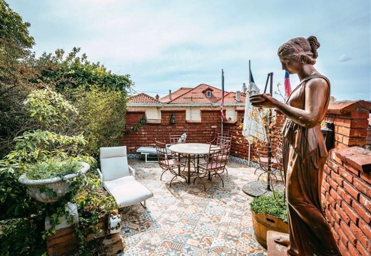 Un patio con una mesa y sillas, rodeado de muros de ladrillo y vegetación.