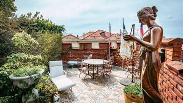Un patio con una mesa y sillas, rodeado de muros de ladrillo y vegetación.