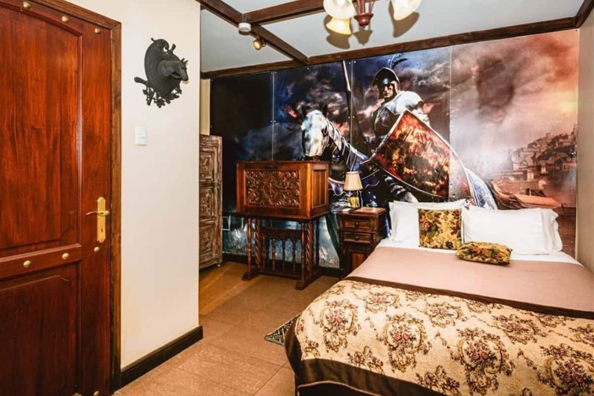 Un dormitorio con una cama, una puerta de madera, un escudo en la pared y un cuadro grande enmarcado.