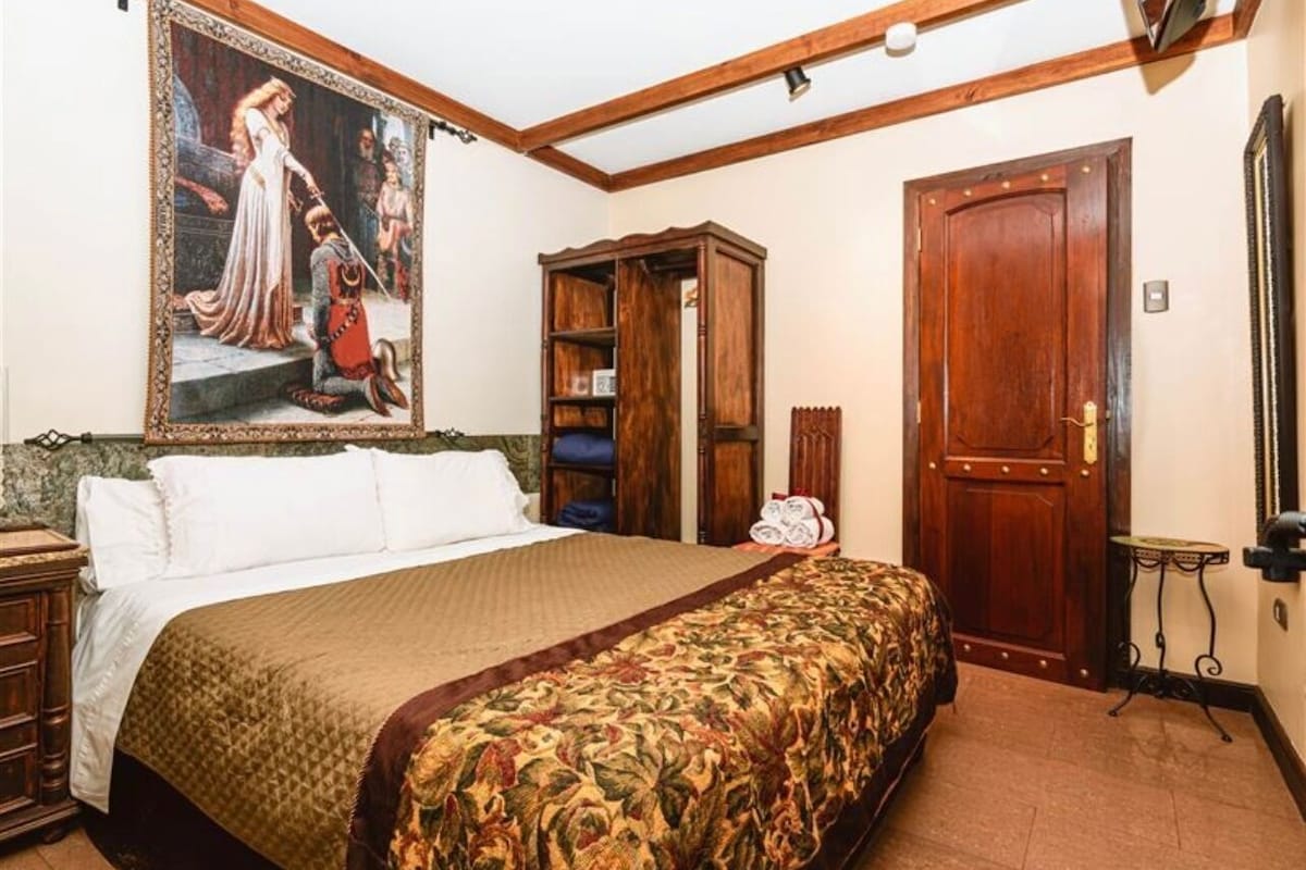 Een slaapkamer met een groot bed, een houten garderobe, een deur en een schilderij aan de muur.
