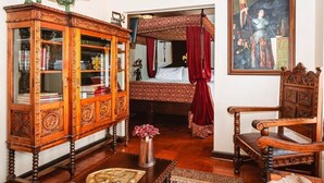 Una habitación con un armario de madera, una cama con cortinas rojas, una silla y un cuadro en la pared.