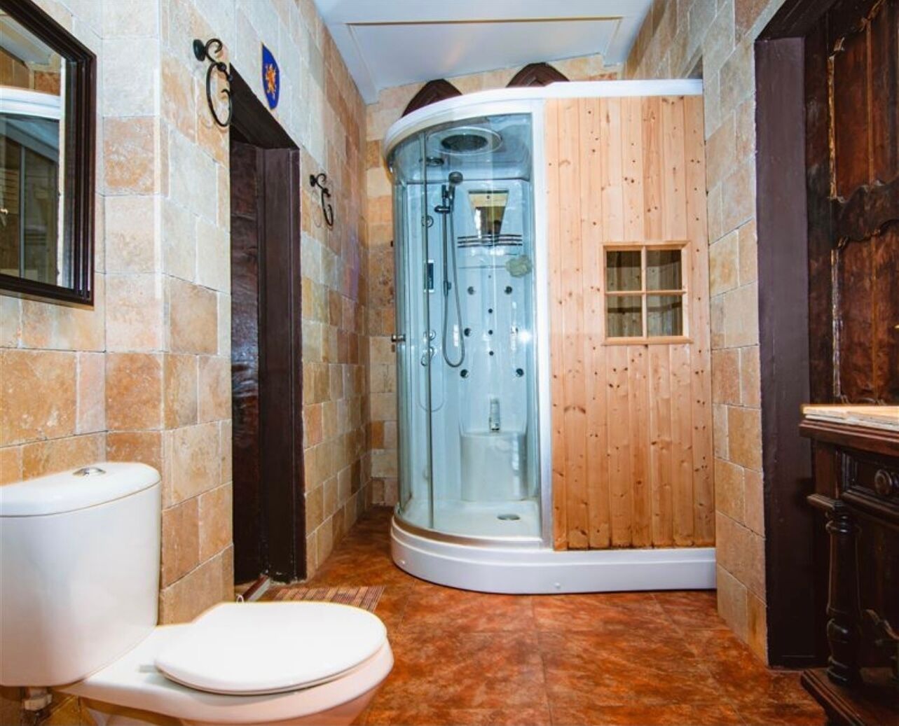 Un baño con ducha envuelta en vidrio, inodoro y puerta de madera.