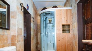 Un baño con ducha envuelta en vidrio, inodoro y puerta de madera.