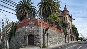 Edificio de piedra histórico con una torre, palmeras y cielo despejado.