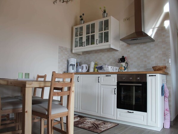 A kitchen with white cabinets, a wooden dining table with chairs, a coffee maker, and an oven.