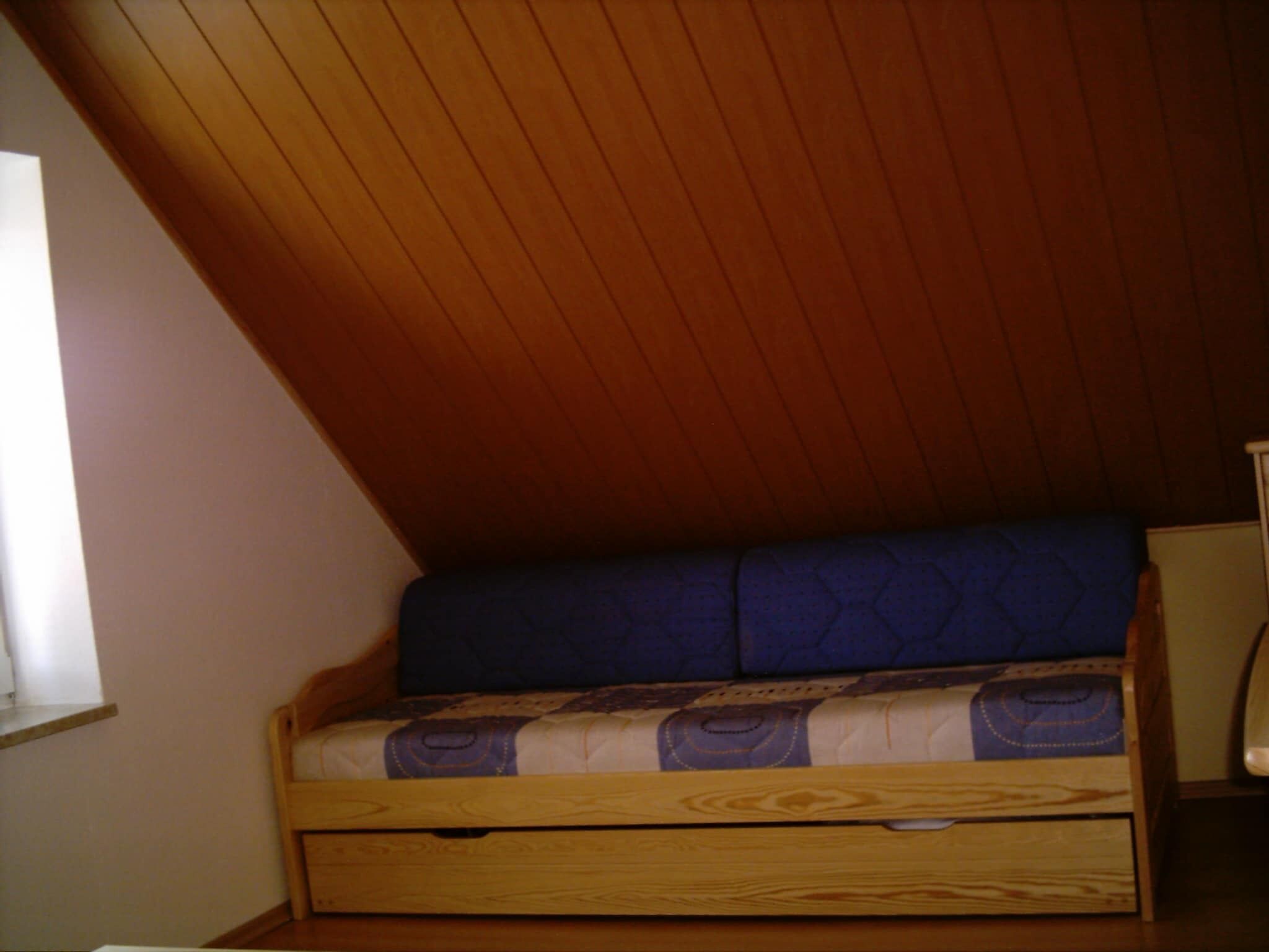 A small, wooden-framed bed with a blue mattress in a room with sloped wooden ceilings.