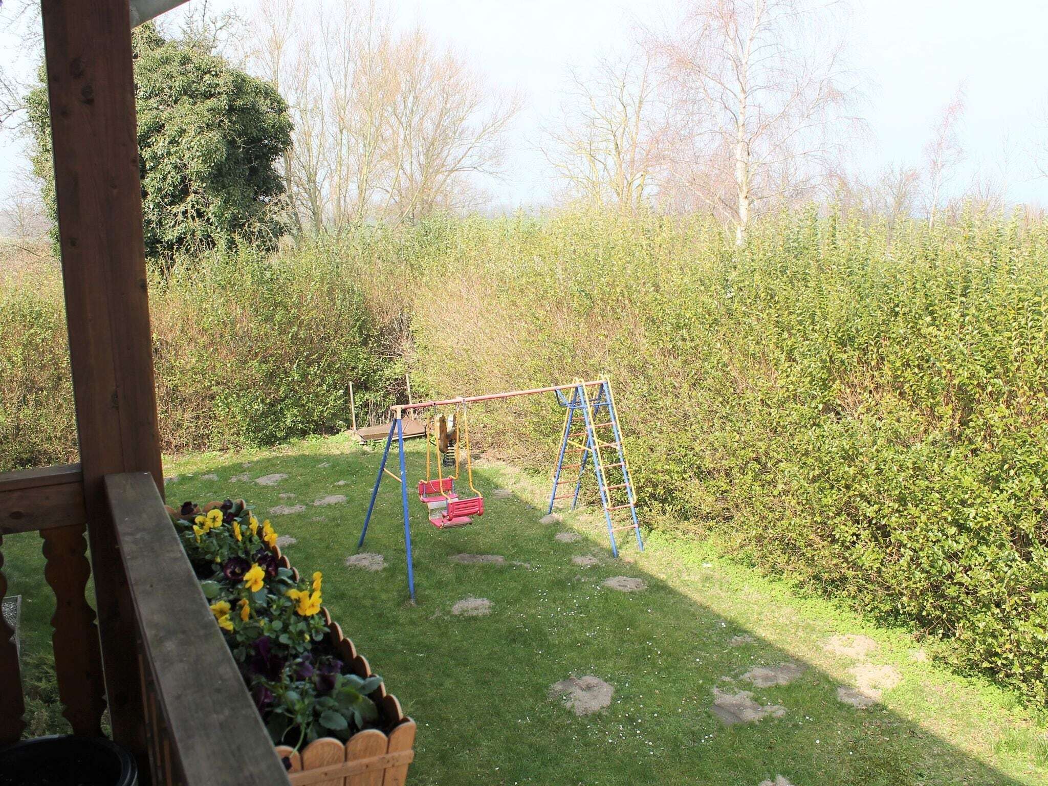 A wooden deck with a swing set and a flower bed.