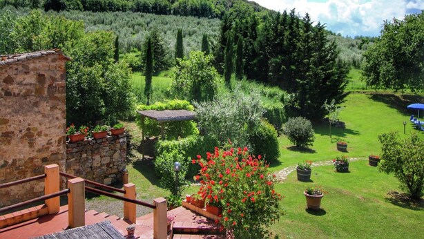 Un giardino con un muro in pietra, una panchina di legno e diverse piante e alberi.