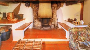 Un interno rustico con un camino tradizionale, travi in legno e pavimento piastrellato.