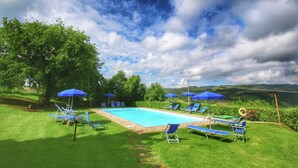 Una piscina con ombrelloni blu e lettini da relax, circondata da erba verde e alberi.