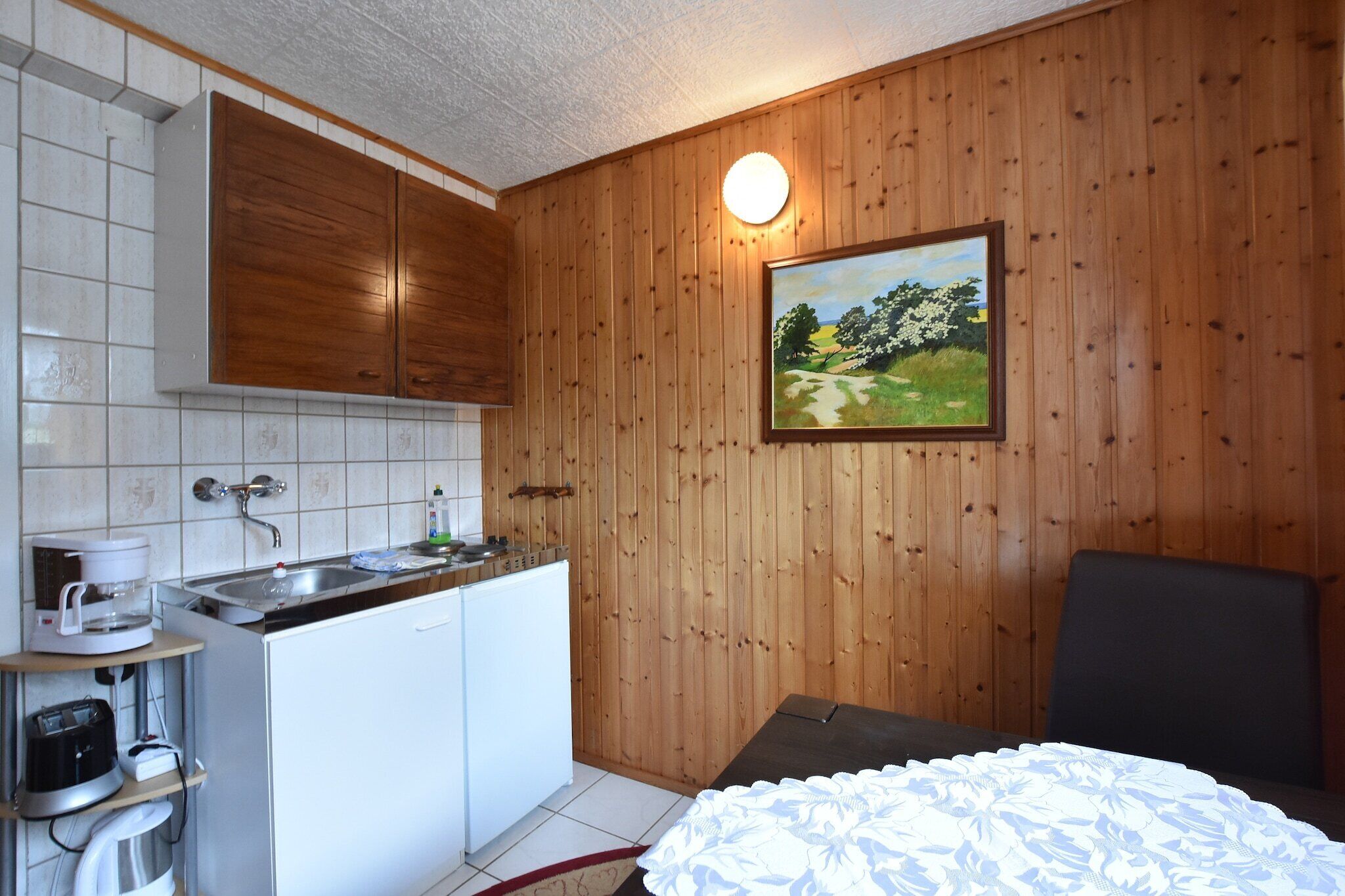 A compact room with a kitchenette, a bed, and a painting on the wall.