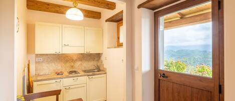 Una cocina con vigas de madera, armarios blancos, una mesa de madera y vistas a un paisaje montañoso a través de una ventana.
