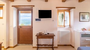 Una habitación con puerta de madera, ventana con vistas, televisor montado, radiador y escritorio con una cesta.
