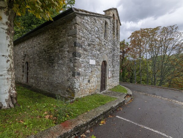 Un edificio de piedra con una pequeña entrada en arco y una puerta, rodeado de césped y árboles.