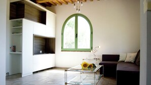 A modern kitchen with white cabinets, a glass-top table, and a window with a green frame.
