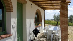 A patio with a grill, white chairs, and a view of a vineyard.