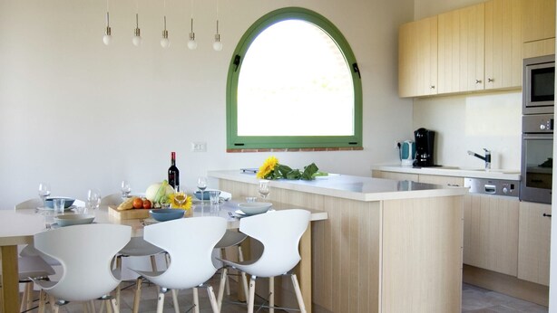 A modern kitchen with a central island, wooden cabinets, and a large window.