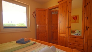 A bedroom with two beds, wooden wardrobes, a window with a view, and a mirror on the wall. - Exklusiver Bungalow mit Terrasse in Rerik (Rerik)