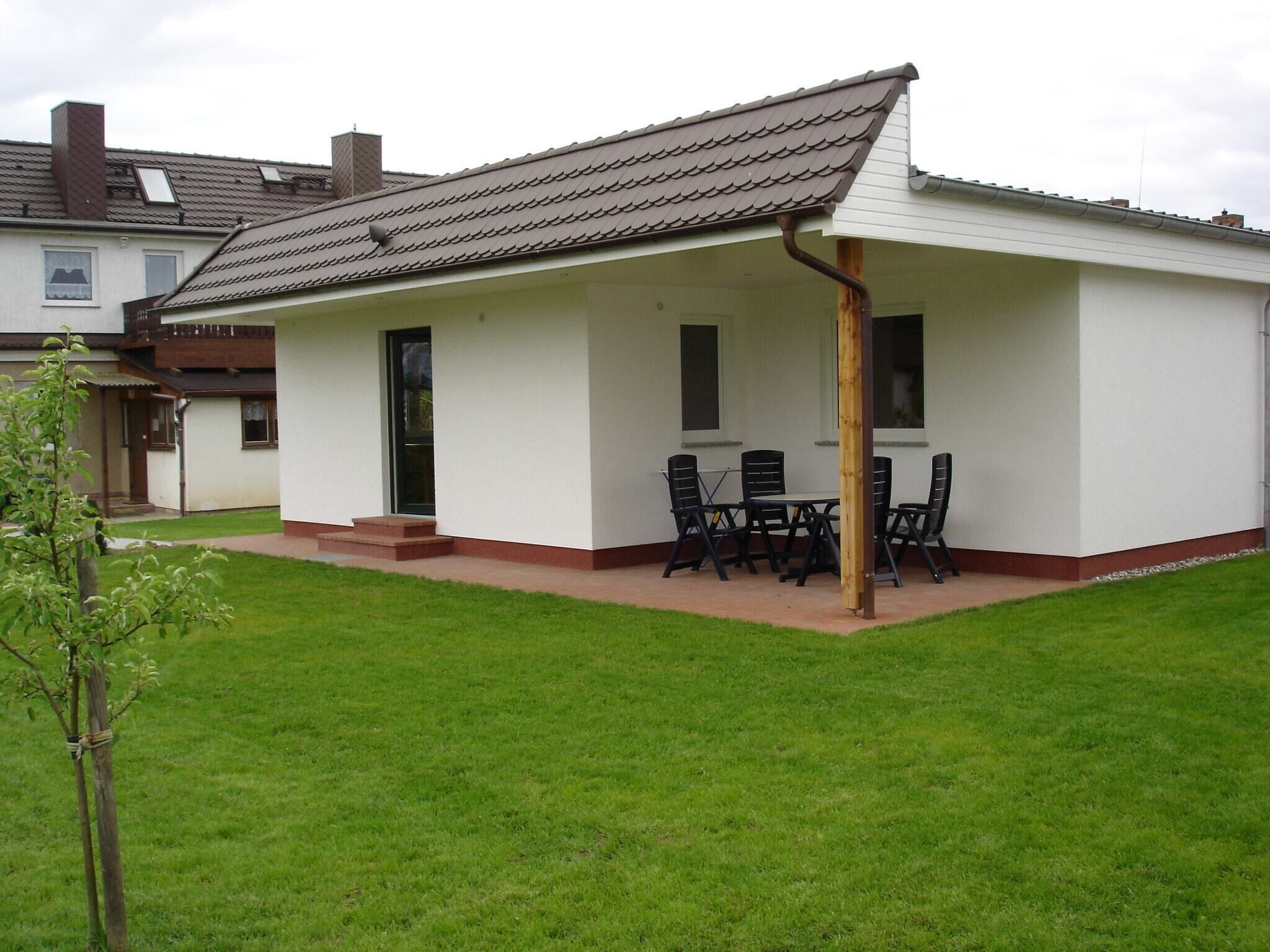 Een gelijkvloers huis met een overdekte patio, een klein gazon en een houten omheining.
