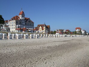 A beach with rows of beach huts labeled WE 10 to WE 17. In the background, there are buildings with red roofs and a prominent building with a tower. - Exklusiver Bungalow mit Terrasse in Rerik (Rerik)