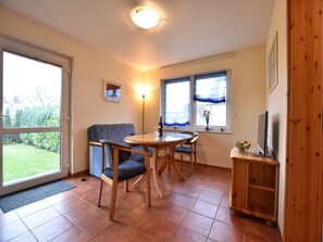 Ein gemütliches Zimmer mit Esstisch, Stühlen, einer Couch, einem Fernseher und einem Fenster mit Vorhängen.
