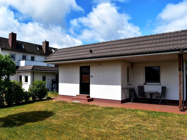 Ein zweistöckiges Haus mit einem Ziegeldach, einer Haustür und einer kleinen Terrasse mit Tisch und Stühlen.