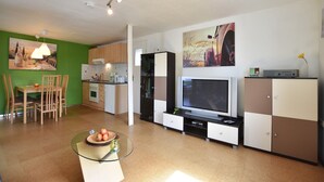 A modern living room with a glass coffee table, a flat-screen TV, and a dining area with wooden chairs and a green wall. - Wohnung in Groß Strömkendorf (Groß Strömkendorf)