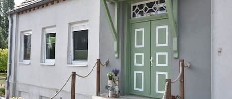 Ein Gebäude mit einer grünen Tür, weißen Fensterrahmen und Steinstufen, die zum Eingang führen.