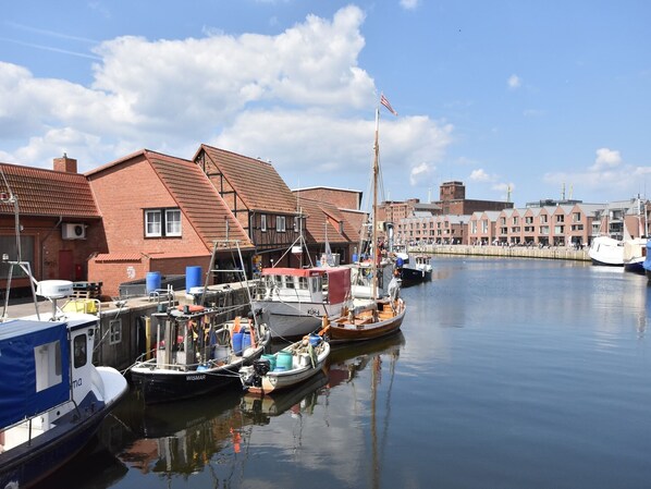 A marina with boats docked, a flag on a flagpole, and buildings in the background. - Wohnung in Groß Strömkendorf (Groß Strömkendorf)