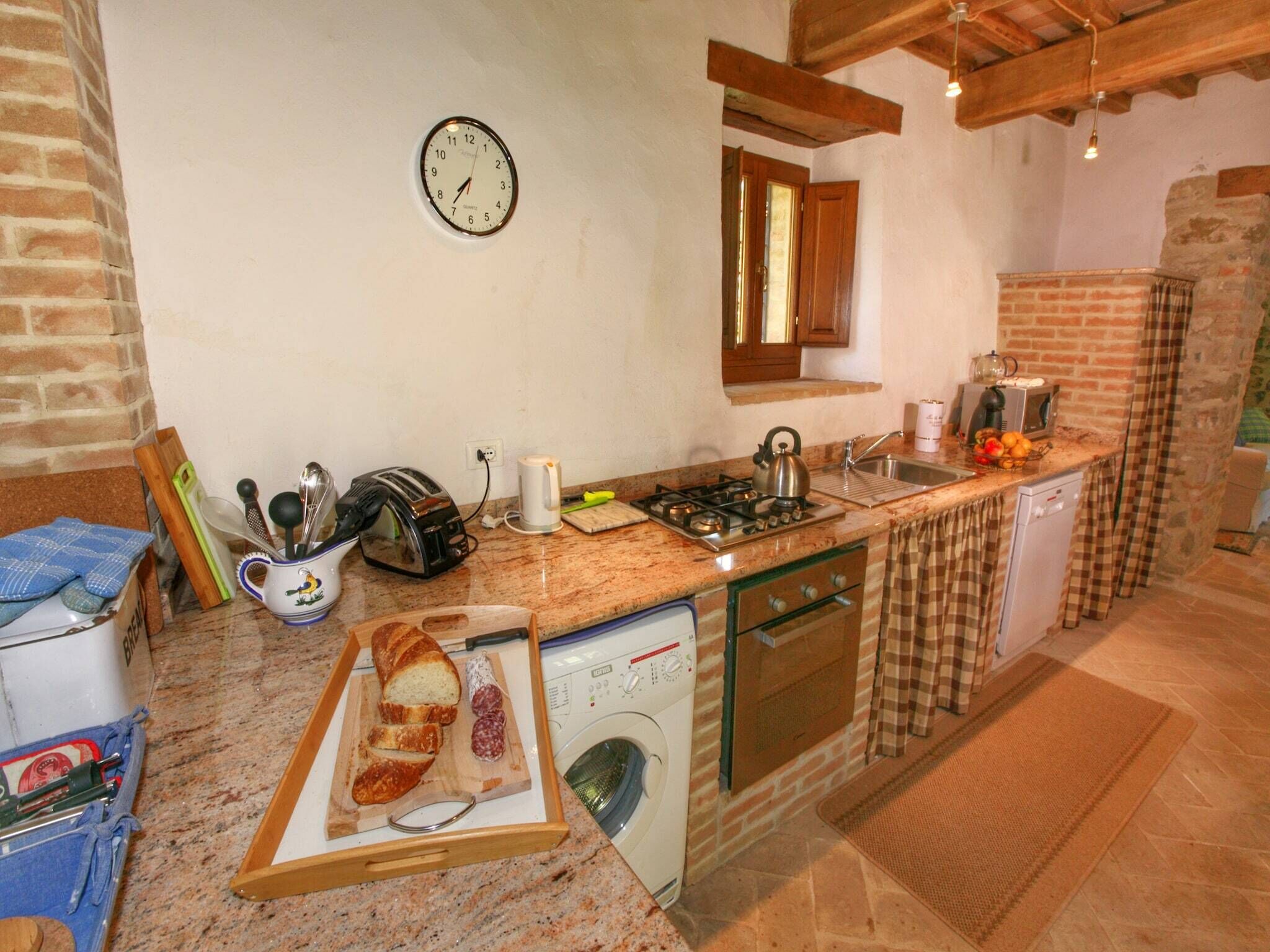A compact kitchen with a built-in oven, a sink, and a clock on the wall.