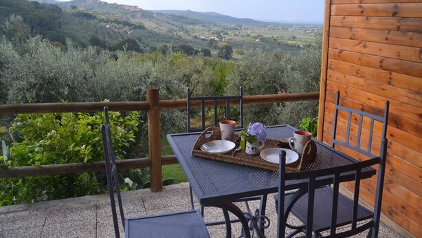 A wooden balcony with a table set for two, overlooking a lush valley. - Charming Tuscan Home Wi-Fi (Castagneto Carducci)