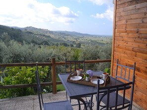 A wooden balcony with a table set for two, overlooking a lush valley. - Charming Tuscan Home Wi-Fi (Castagneto Carducci)
