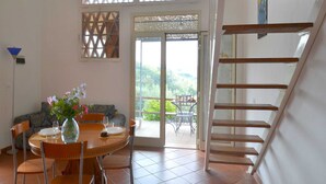 A dining area with a round table, chairs, and a vase of flowers. There is a staircase to the right and a door leading outside. - Charming Tuscan Home Wi-Fi (Castagneto Carducci)