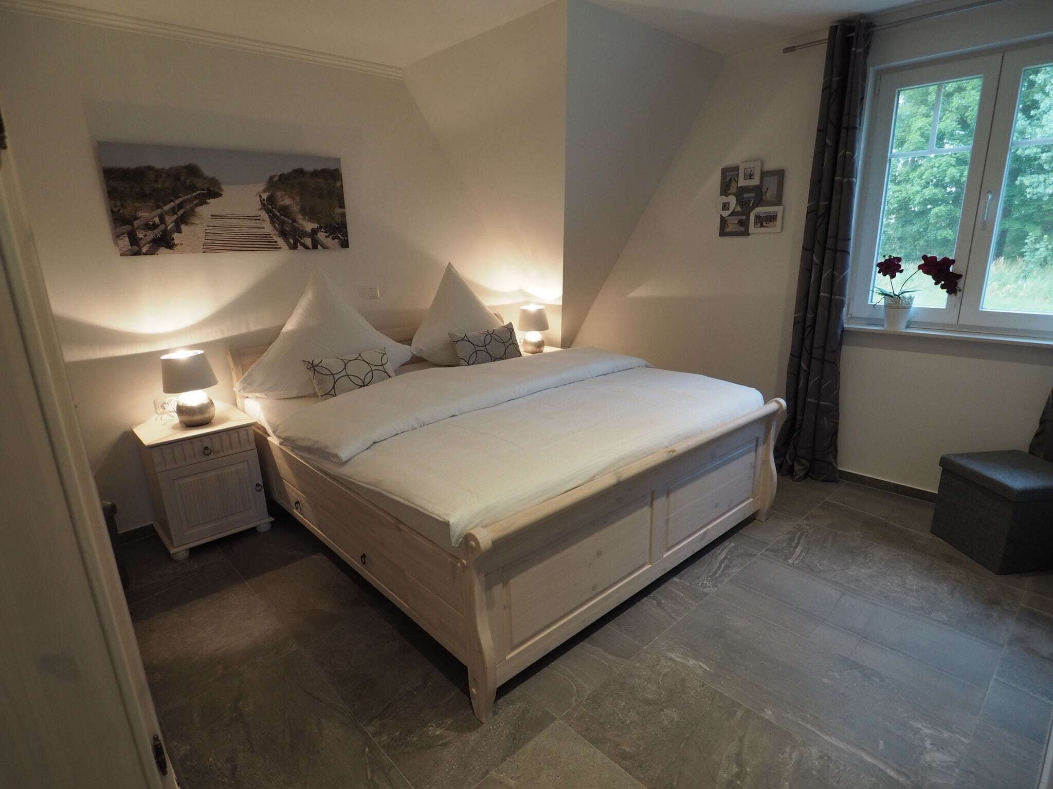 A bedroom with a bed, nightstands, a window with curtains, and wall decorations.