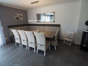 Een eetgedeelte met een houten tafel en rieten stoelen, een spiegel boven de tafel, en een moderne keuken met een fornuis.