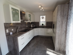 A modern kitchen with white cabinetry, dark countertops, and a built-in stove. - Ferienhaus in Rerik mit Garten (Rerik)