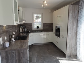 A modern kitchen with white cabinets, a built-in oven, and a window with a view. - Ferienhaus in Rerik mit Garten (Rerik)