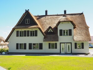 Een tweekamerhuis met rieten dak, witte muren en meerdere ramen met luiken.