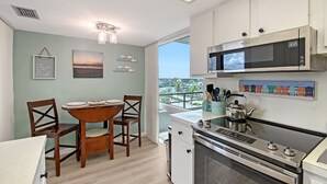 A modern kitchen with a built-in microwave, stove, and oven. There is a dining table with chairs and a view of the city through large windows. - Anchorage 610 (Siesta Key)