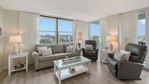 A modern living room with a sofa, two armchairs, a glass coffee table, and a view of the city through large windows. - Anchorage 610 (Siesta Key)