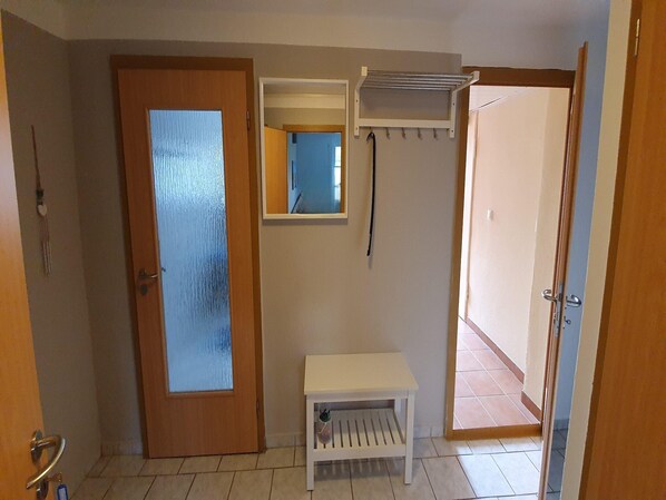 A room with a wooden door, a small white bench, a mirror, and a metal drying rack.