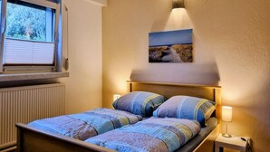 Ein Schlafzimmer mit einem Einzelbett, einem Fenster mit Jalousien, einer Wandlampe und einem Bild über dem Bett.